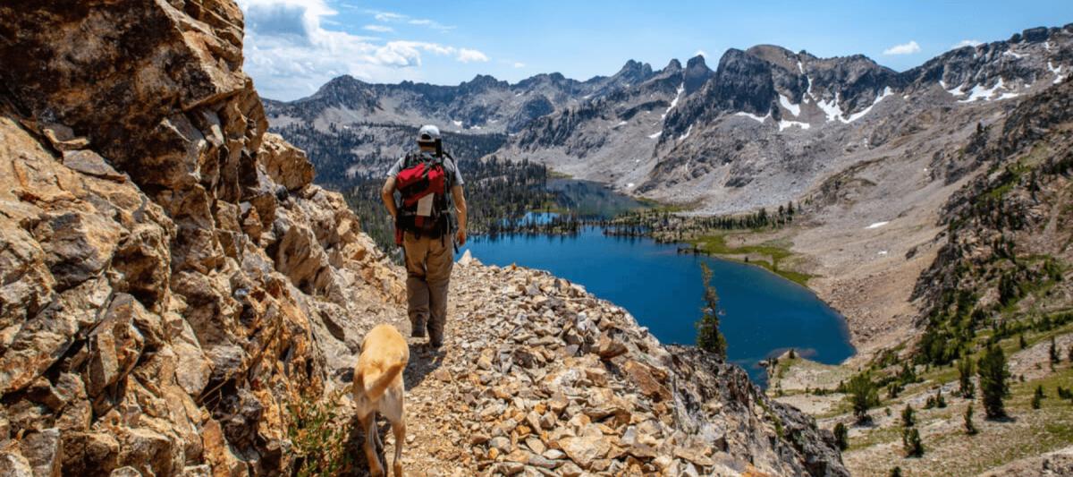Man and dog hiking next to a mountain overlooking a lake